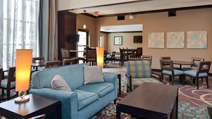 A hotel lobby with a blue sofa, wooden tables, and chairs, a patterned carpet, and artwork on the walls. - 1 Bedroom | Pool & Gym. Free Breakfast (O'Fallon)