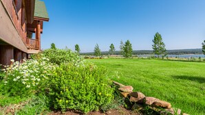 A wooden cabin with a balcony overlooking a grassy area and a lake.