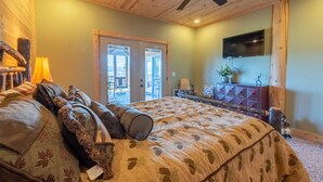 A bedroom with a large bed, wooden ceiling, and a TV mounted on the wall.