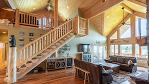 A spacious living area with a wooden staircase, a large television, and a cozy seating arrangement.