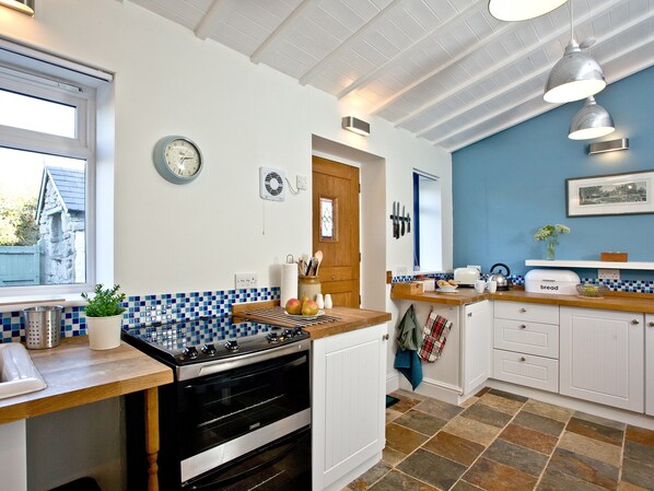 A kitchen with a stove, oven, and a blue tiled backsplash. - 2 bedroom accommodation in Pendeen (Pendeen)