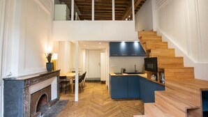 A modern interior with a fireplace, dining area, kitchen, and a wooden staircase. - Le Chavannes-Ecrin élégant & Cosy- Pentes X Rousse (Lyon)