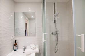 Casa de banho moderna com cabine de chuveiro em vidro, lavatório branco com uma garrafa de champô e um espelho.
