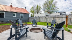 Une terrasse extérieure avec quatre fauteuils Adirondack et un foyer.