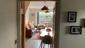 Une porte qui donne sur un salon, où se trouvent un canapé, des fauteuils, une table et un luminaire suspendu.