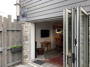 A residential entryway with a stone wall, a wooden fence, and a sliding glass door leading to a living area with a television, a wooden table, and a rocking chair.