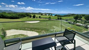 Un balcon avec vue sur un terrain de golf, une zone sablonneuse et un ciel bleu dégagé.