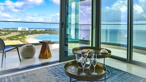 Ein Balkon mit Blick auf das Meer und den Strand, ein Tisch mit einer Champagnerflasche und ein Stuhl.