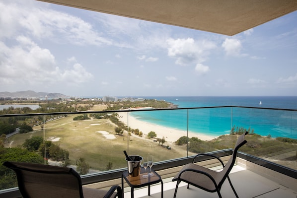 A balcony with two chairs and a table, overlooking a beach and ocean.
