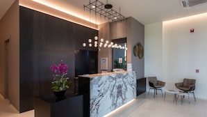 Un área de recepción moderna con mostrador de mármol, iluminación colgante y dos sillones.