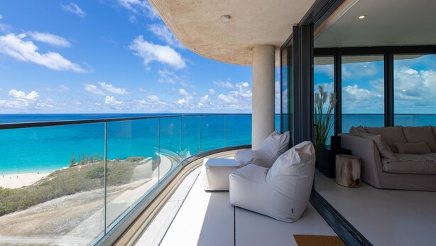 Ein Balkon mit Blick auf den Ozean und den Strand, ein weißes Sofa und ein kleiner Tisch.
