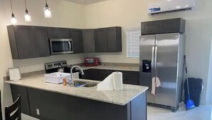 Eine moderne Küche mit dunklen Schränken, einem Edelstahlkühlschrank, einer Mikrowelle und einer Arbeitsplatte aus Granit.
