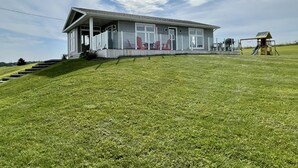 Une maison avec un porche, une petite terrasse et un espace de jeux pour enfants avec un toboggan.