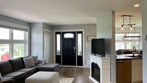 Un salon moderne avec un canapé d’angle, une cheminée et un coin cuisine équipé d’un téléviseur.