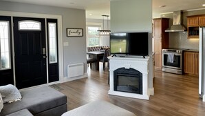 Un salon moderne avec une cheminée, un téléviseur et un coin repas à l’arrière-plan.
