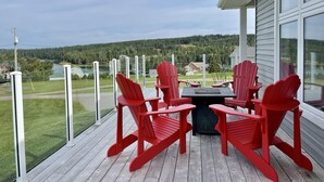 Une terrasse en bois avec une table et quatre chaises Adirondack rouges, donnant sur un lac et des collines boisées.