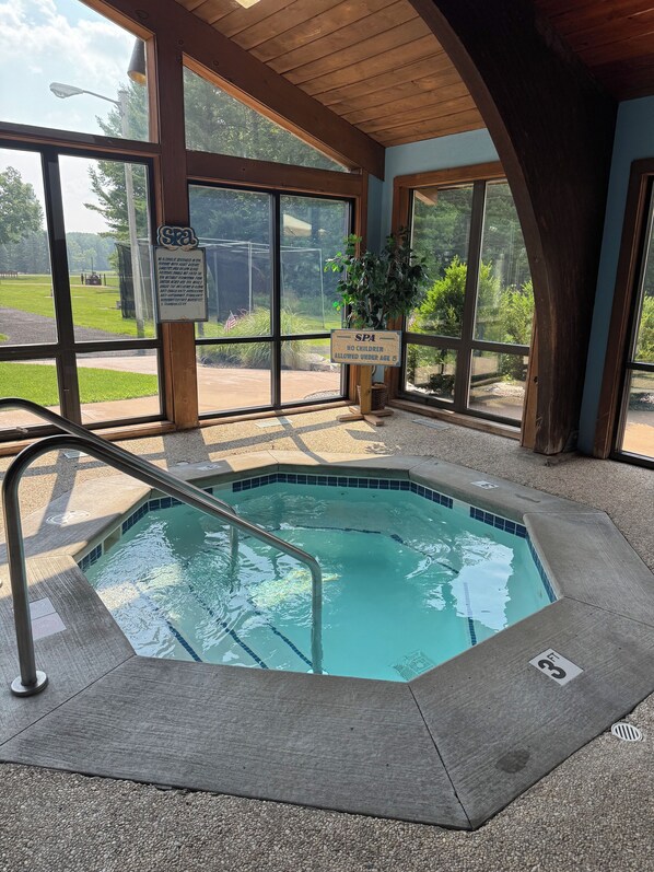 Ein Spa-Bereich mit Whirlpool, Holzbalken und großen Fenstern mit Blick auf eine grüne Landschaft.