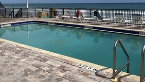 Piscina con vista al océano, rodeada de sillas de descanso y una valla.