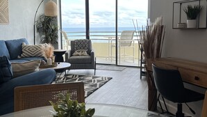 Una sala de estar moderna con un ventanal grande, un sofá, una mesa de comedor y un espacio de trabajo con una computadora.