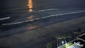 Un atardecer sobre el océano, con un estacionamiento y palmeras al frente.