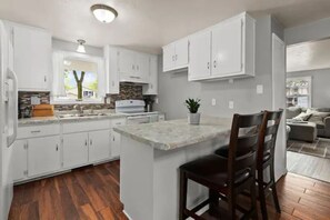 A modern kitchen with white cabinets, a central island, and a wooden floor.
