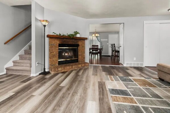 A living room with a fireplace, a staircase, and a dining area.