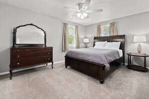 Een slaapkamer met een bed, dressoir, nachtkastje en plafondventilator.