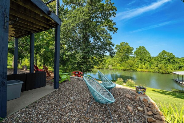 A covered outdoor seating area with chairs and kayaks, overlooking a lake with trees and a clear sky.