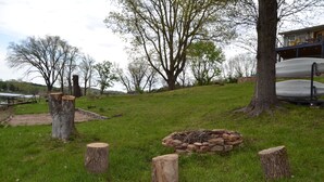 A grassy outdoor area with a fire pit, wooden stumps, and a large tree.