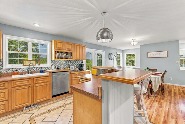A spacious kitchen with wooden cabinets, a central island, and a dining area with a table and chairs. - Lakefront, private dock on cove near HaHa Tonka, Ballparks National Park, kayaks (Camdenton)