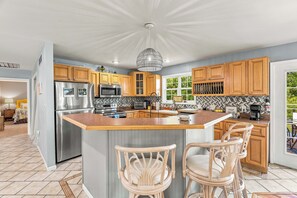 A modern kitchen with a central island, stainless steel appliances, wooden cabinets, and a herringbone tile backsplash.