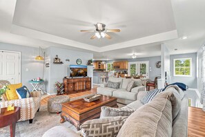 A spacious living room with a large sofa, a coffee table, and a television. There is a kitchen area visible in the background. - Lakefront, private dock on cove near HaHa Tonka, Ballparks National Park, kayaks (Camdenton)