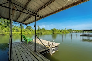 A wooden dock extending into a calm body of water, with a green chair and a small boat docked at the end. - Lakefront, private dock on cove near HaHa Tonka, Ballparks National Park, kayaks (Camdenton)