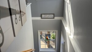 A staircase with wooden steps, a small window with a sailboat painting, and a sign above the window that reads "LAKE HOUSE".
