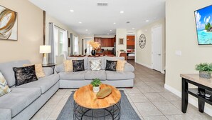 A modern living room with a grey sectional sofa, a round coffee table, and a dining area with a small table and chairs. - Fun and Stylish Family Villa in Encore Resort! (Kissimmee)