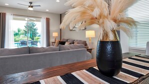 A modern living room with a sofa, a large vase with pampas grass, and a dining table with a striped placemat. - Fun and Stylish Family Villa in Encore Resort! (Kissimmee)