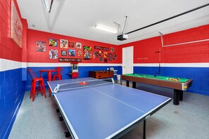 A room with a ping pong table, red and blue walls, and a pool table.