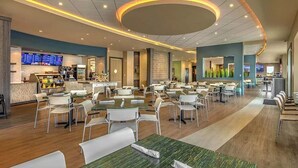 A spacious hotel dining area with multiple tables and chairs, a central bar, and a digital menu display. - Fun and Stylish Family Villa in Encore Resort! (Kissimmee)