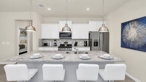 Une cuisine moderne avec des armoires blanches, des comptoirs en granit, des appareils électroménagers en acier inoxydable et des luminaires suspendus.