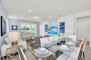 A modern dining area with a glass table set for six, surrounded by white chairs.