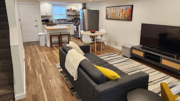 Een moderne woonkamer met een grijze bank, een televisie en een eethoek met een tafel en stoelen.