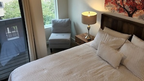 Een hotelkamer met een groot bed, een nachtkastje met lamp, een stoel en een raam met uitzicht op groen.