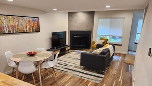 Een moderne woonkamer met een flatscreen televisie, een open haard, een eethoek met een tafel en stoelen, en een bank.