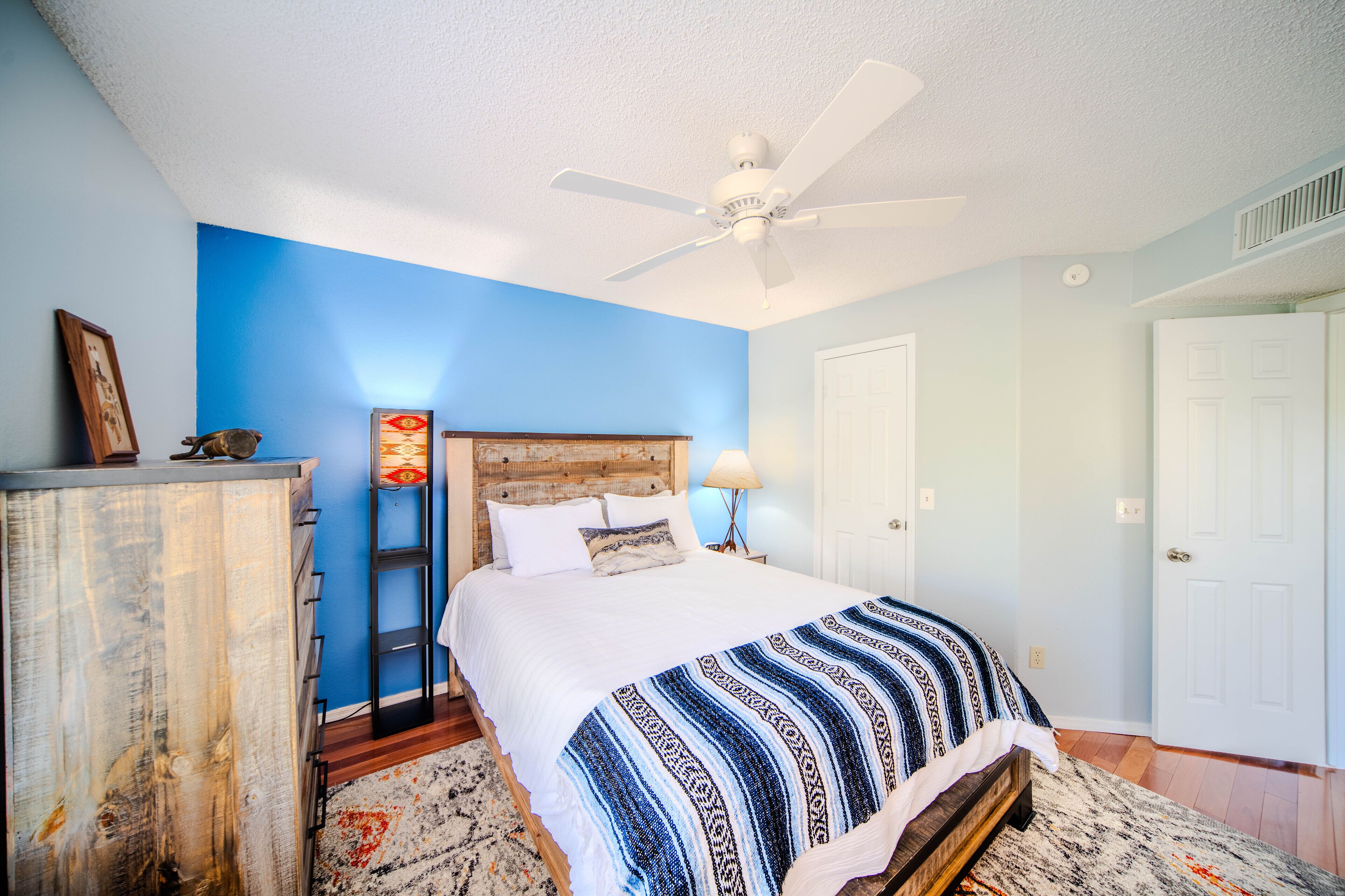 A bedroom with a bed, a ceiling fan, a dresser, and a nightstand.
