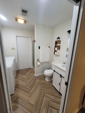 A bathroom with a toilet, sink, and a mirror. There is a towel hanging on a rack and a shower door.