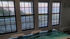 A room with a large window, a wooden table with a painted ocean scene, and a ceiling light fixture.