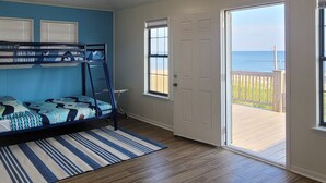 A room with bunk beds, a ceiling fan, a door leading to a balcony with a view of the ocean, and a star-shaped light fixture on the ceiling.