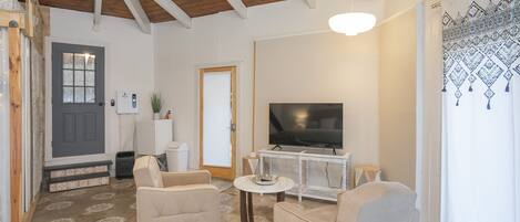 Un salón espacioso con un televisor grande, dos sillones color beige, una mesa de centro y un techo de madera.
