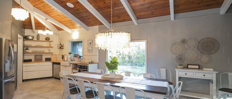 A spacious kitchen with white cabinetry, a wooden ceiling, and a large dining table with chairs.