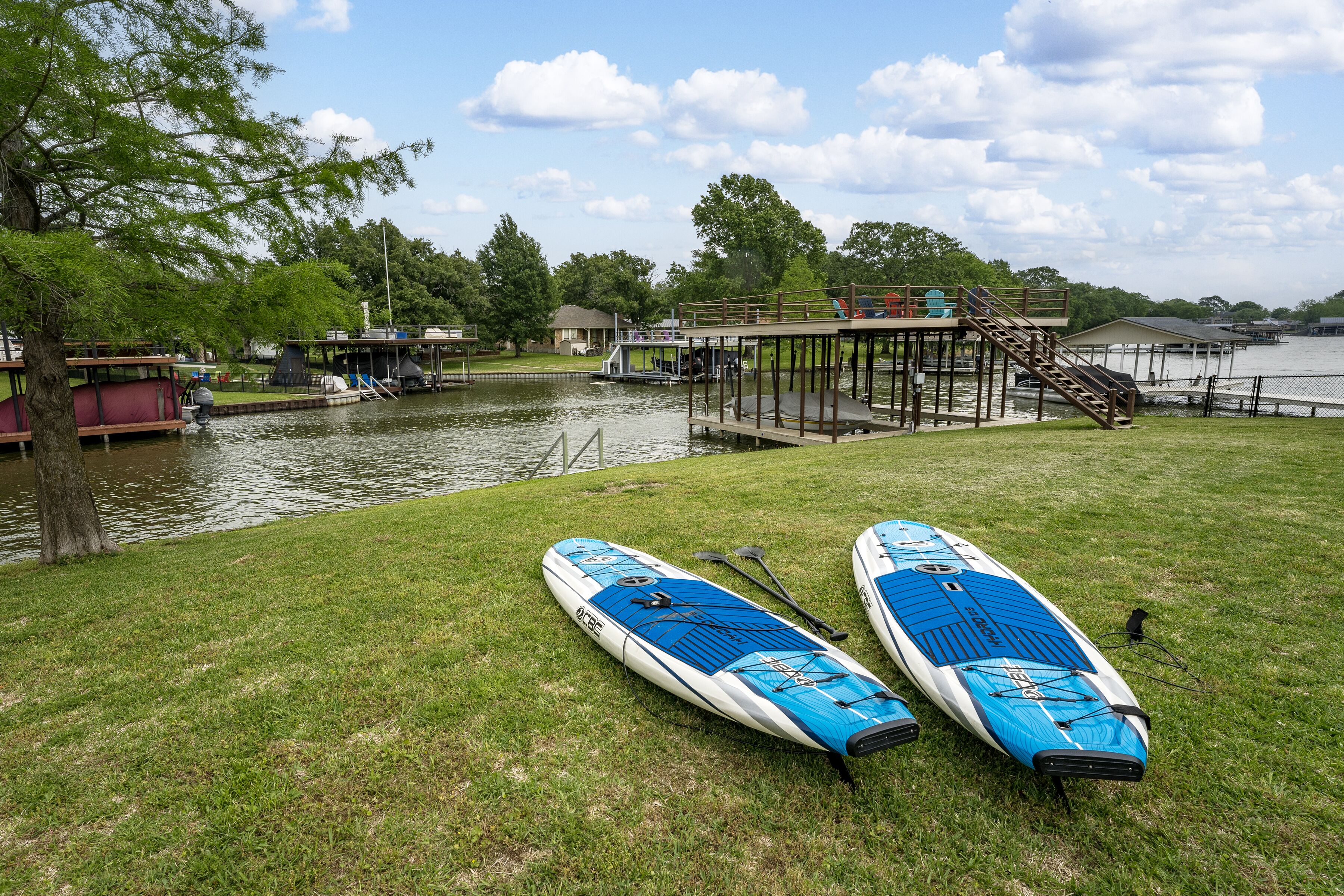 A grassy area with two paddleboards and a dock extending into a body of water.